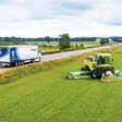 Lkw mit Krone-Trailer fährt auf der Straße, ein Mähdrescher von Krone verrichtet seine Arbeit auf dem Feld