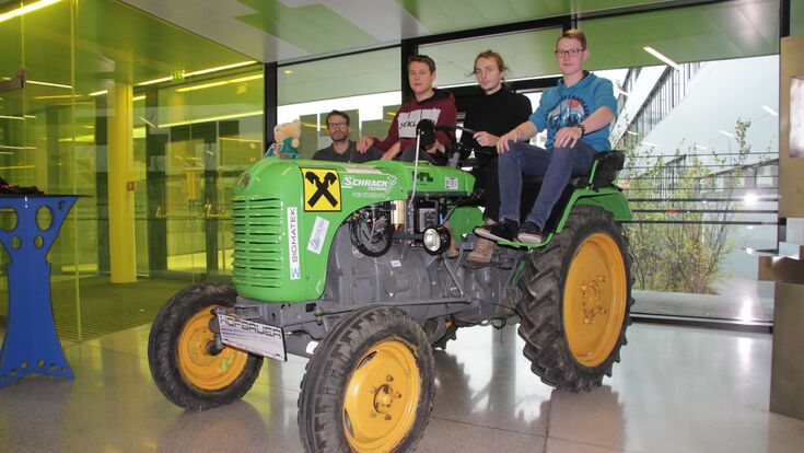 elektrifizierter 18er-Steyr-Traktor im Foyer der HTL St.Pölten. Schüler sitzen darauf, Lehrer steht daneben