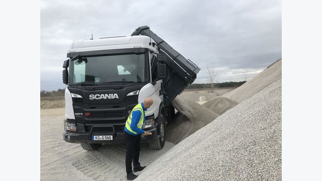 Lkw kippt seitlich ab, Fahrer steht mit Fernbedienung daneben