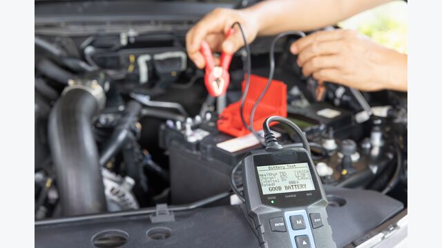 Man is measuring AGM battery power of suv car by battery tester at home.